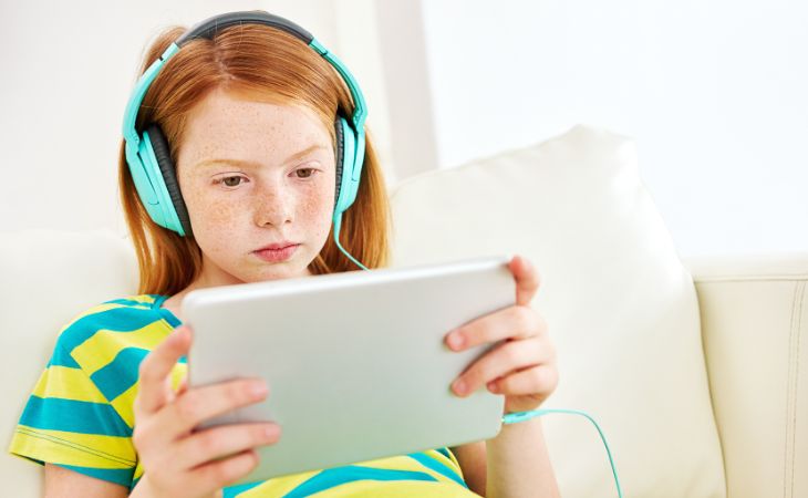 How to prevent children from becoming addicted to screens: A girl sitting with a tablet and headphones