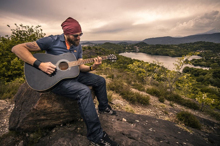 Small parental gestures for children: A bearded man sitting on a tree stump in nature, playing a guitar