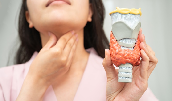 Tonsil cancer: a woman holding her throat next to a model of a lymph node