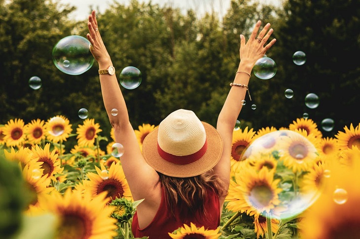 Fears of people-pleasers: a young woman standing in a sunflower field and raising her arms